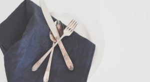 gray fork, spoon, and butter knife on plate with black table napkin